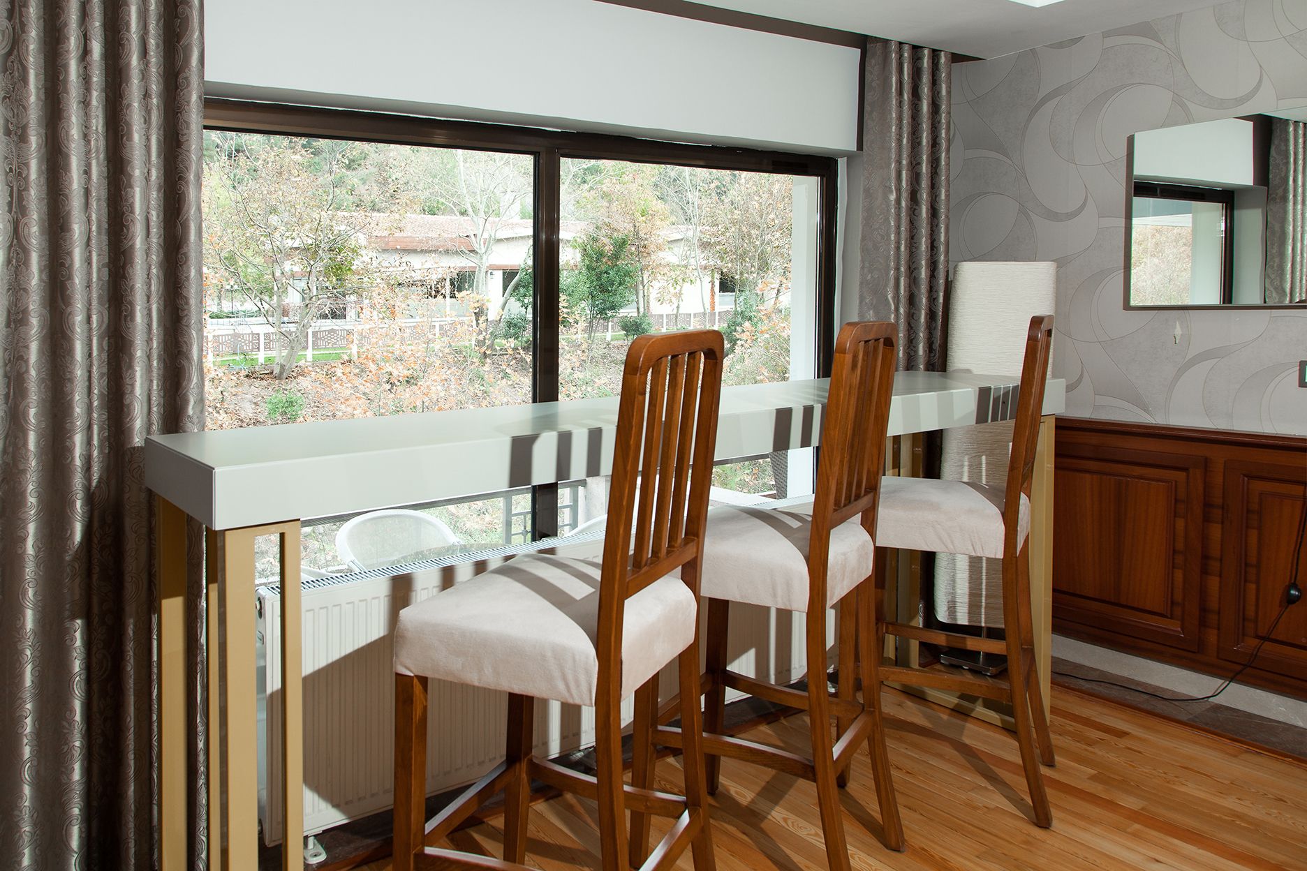A kitchen with wooden chairs, a white countertop, and a window with curtains.
