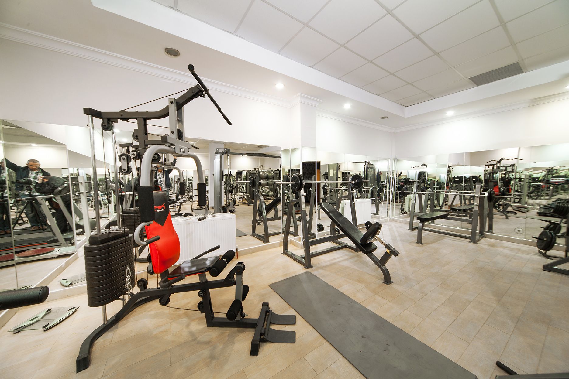 Uma academia com diversos equipamentos de exercícios, incluindo máquinas de musculação e pesos livres, dispostos em um espaço amplo.