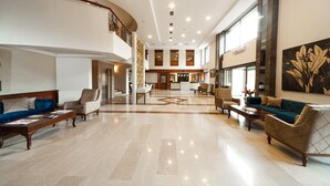 Um hall amplo com teto alto, pisos de mármore polido e área de estar central com sofás e poltronas.