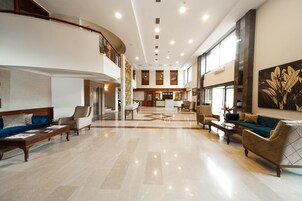 Un vestíbulo espacioso con techo alto, pisos de mármol pulido y una zona de estar central con sofás y sillones.