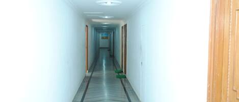 A long, narrow hallway with a patterned floor, white walls, and wooden doors on either side.