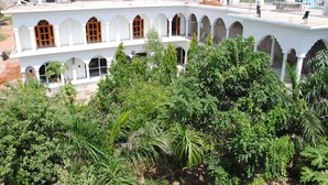 A white building with multiple arched windows and a courtyard surrounded by greenery. - Hotel Isabel Palace (Rajnagar)