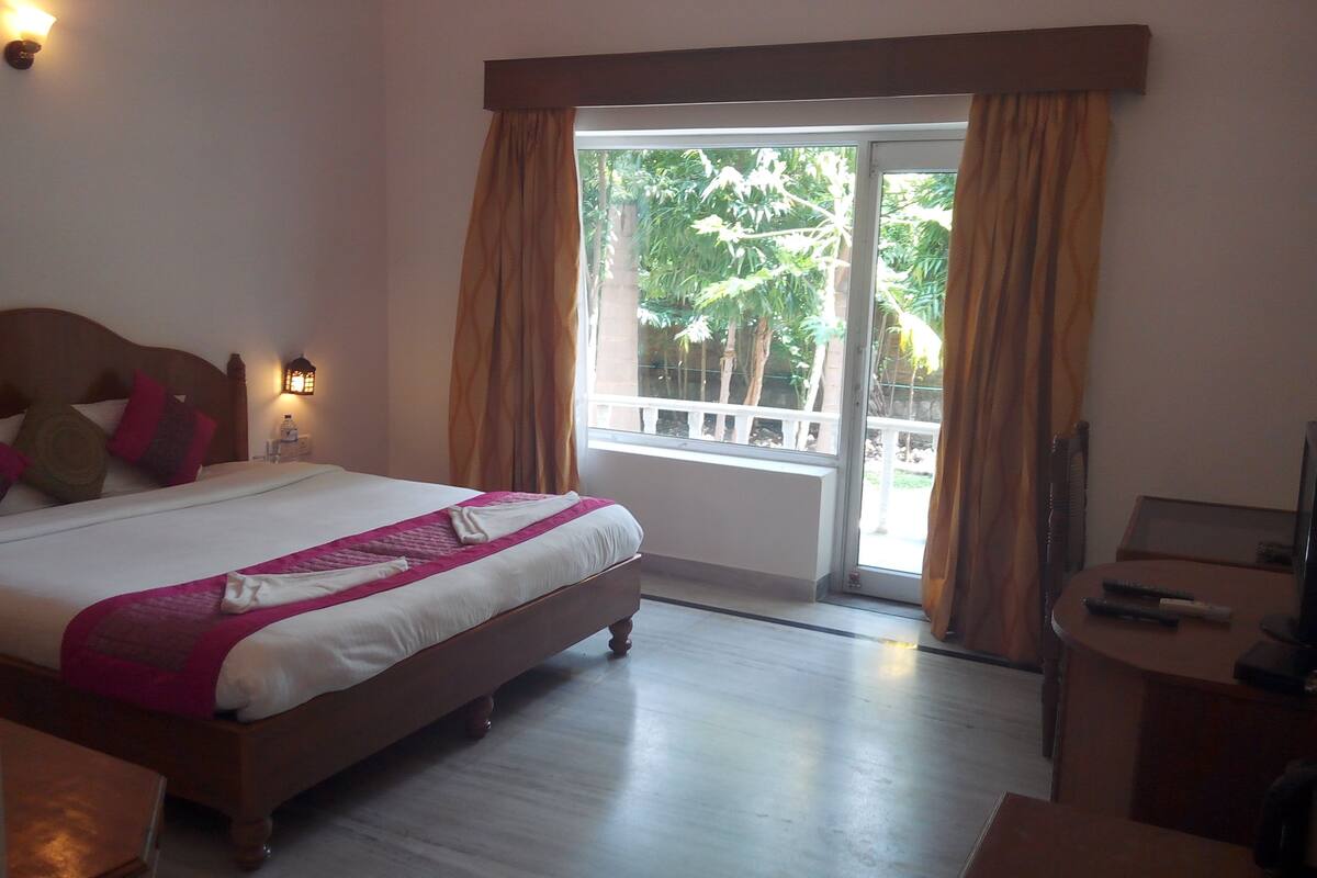 Una habitación de hotel con una cama grande, una mesita de noche con una lámpara, un escritorio y vistas al exterior a través de una puerta corredera.