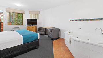 A hotel room with a bed, a desk, a chair, a TV, and a bathtub.