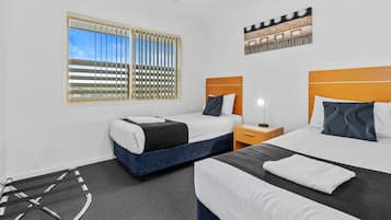 A hotel room with two beds, a window with blinds, a ceiling fan, a nightstand, and a wall-mounted artwork.