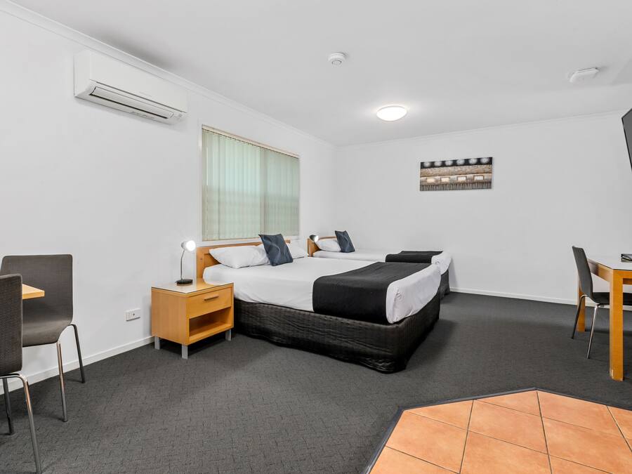 A hotel room with a bed, bedside table, lamp, chair, desk, and a television.