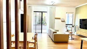 A modern living room with a sofa, TV, and exercise bike. - Parkview Apartments (South Brisbane)