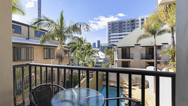 A balcony with a glass table and chairs, overlooking a swimming pool and a cityscape. - Parkview Apartments (South Brisbane)
