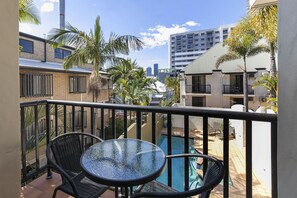 Ein Balkon mit Glastisch und Stühlen, der auf einen Pool und die Skyline blickt.