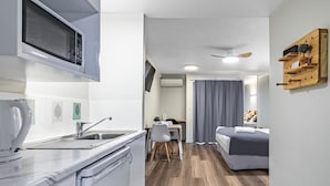 A compact kitchen with a microwave, sink, and modern appliances. A dining area with a table and chairs is visible, leading to a bedroom with a bed and a ceiling fan. - Parkview Apartments (South Brisbane)