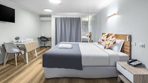 A modern hotel room with a bed, bedside table, desk, chair, and a TV. - Parkview Apartments (South Brisbane)