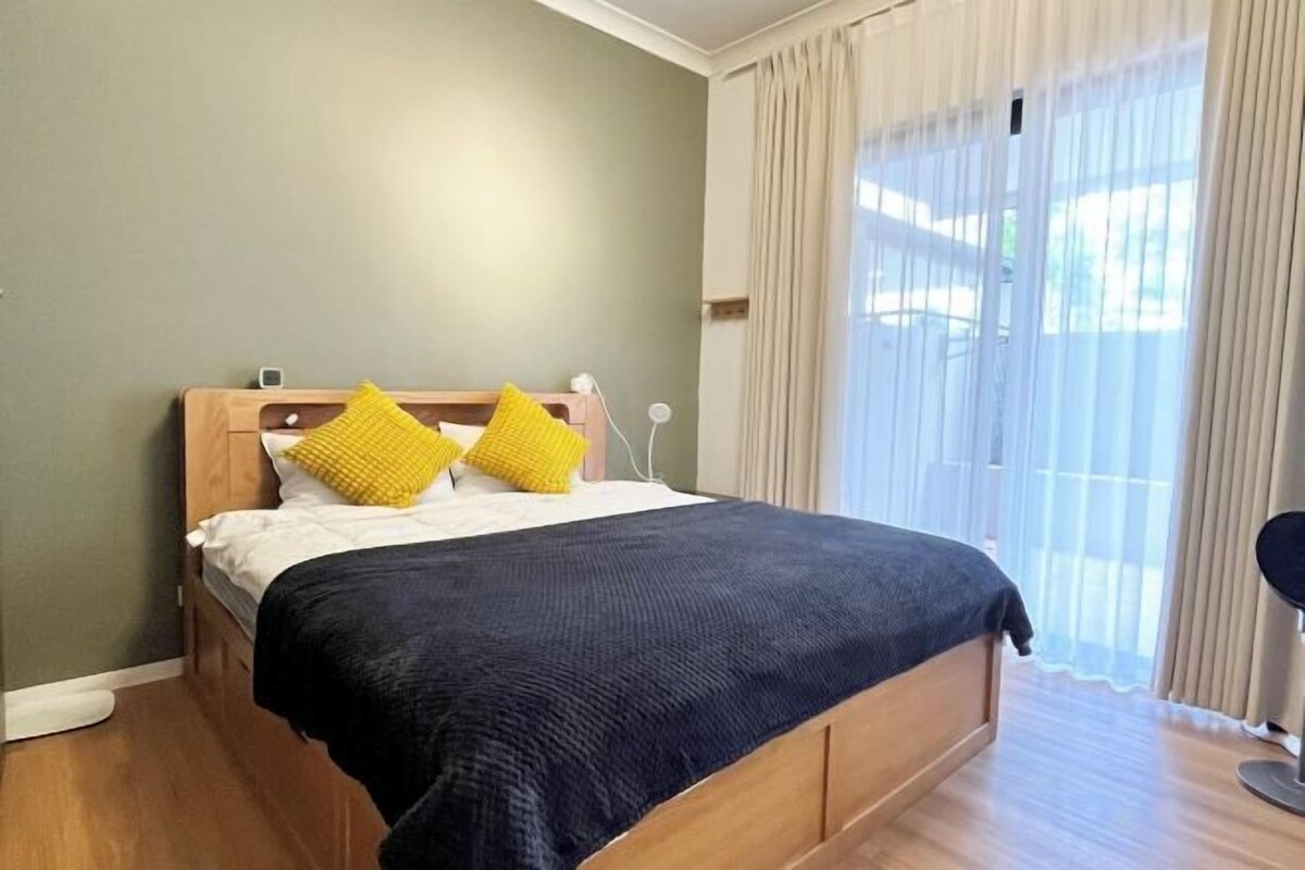 A bed with a wooden frame, two pillows, a dark blanket, and a bedside table with a lamp.
