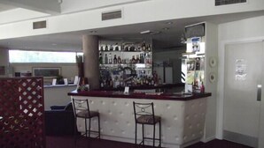 A bar area with two stools, a bar counter, and a shelf with various bottles. - River Park Motor Inn (Casino)