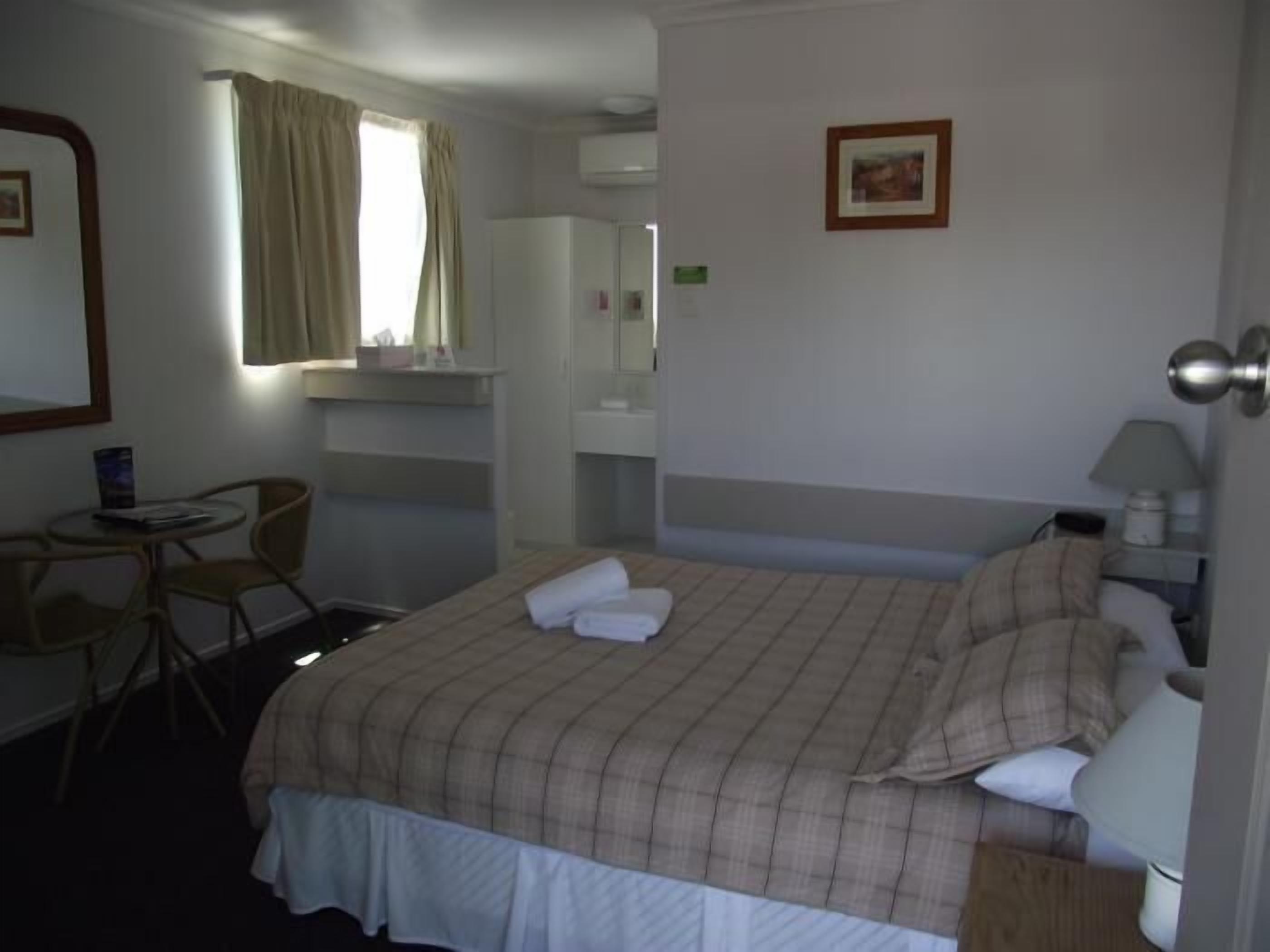 A hotel room with a bed, a desk, a chair, a wardrobe, a mirror, and a window with curtains.