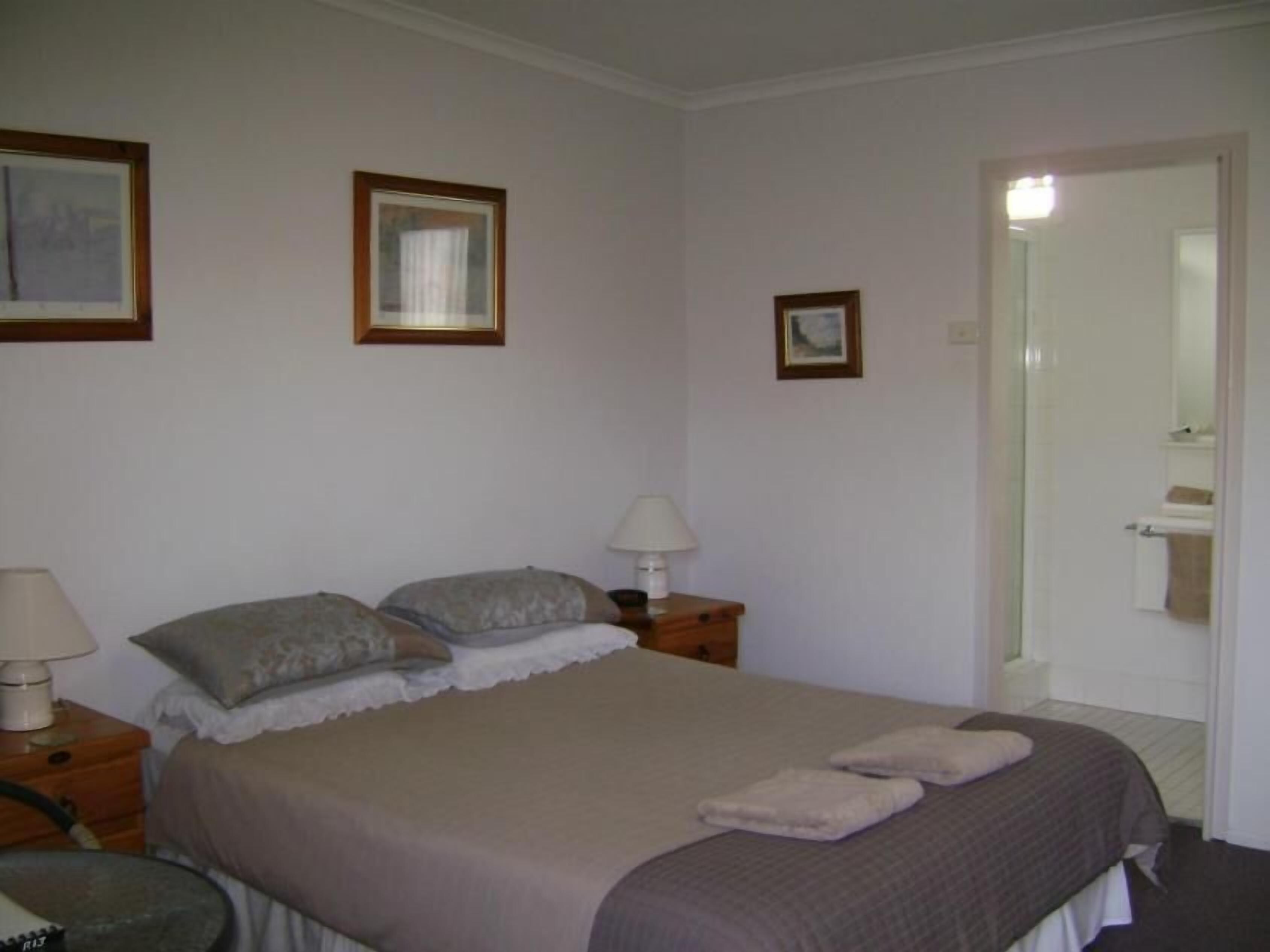 A bedroom with a bed, two bedside tables with lamps, a mirror, and a door leading to a bathroom.