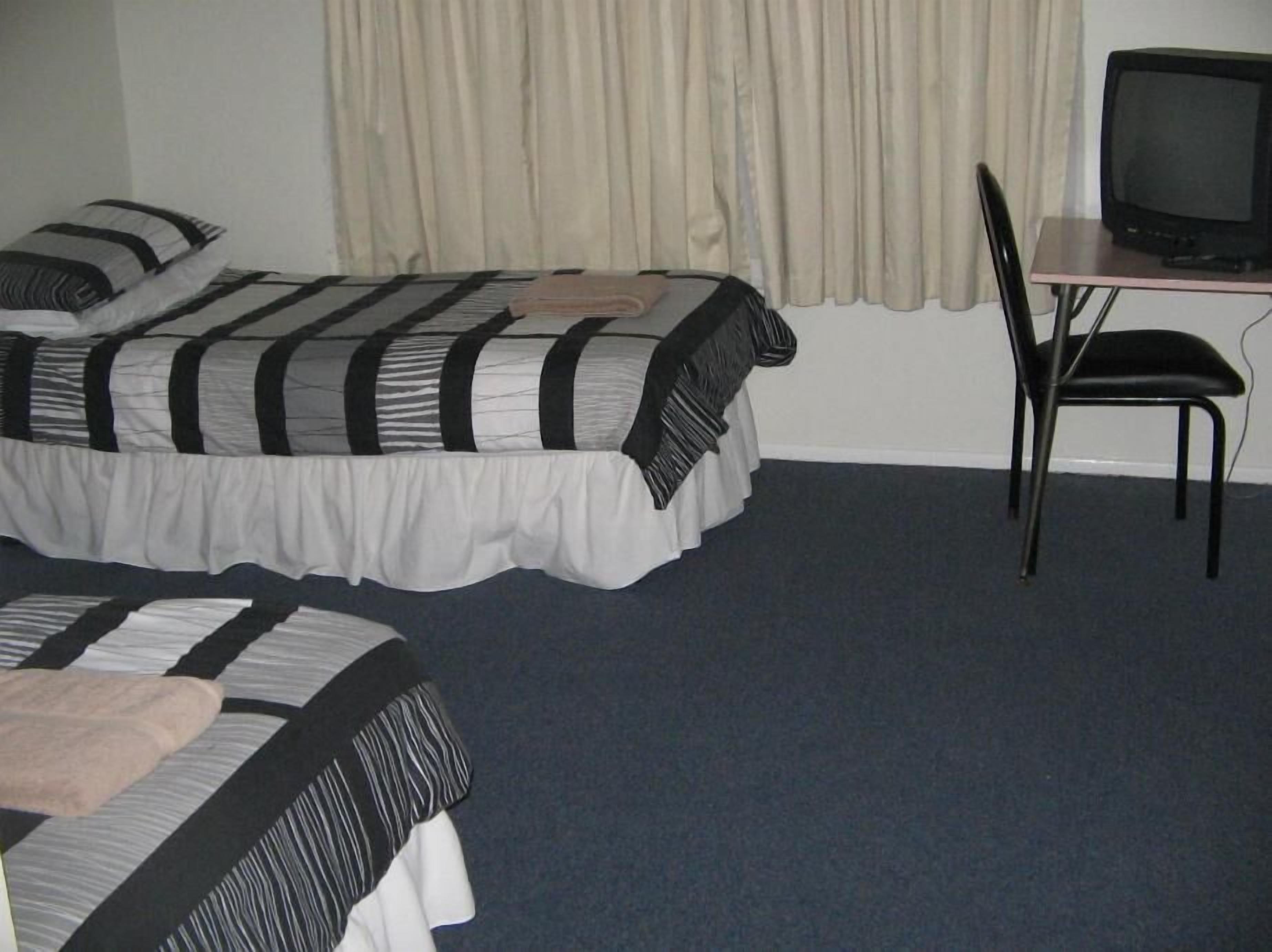 A room with two beds, a desk with a television, and a chair.