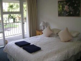Quarto com cama, almofadas, mesa de cabeceira, abajur e um quadro na parede.