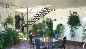 An outdoor patio area with a round table and chairs, surrounded by potted plants and a staircase. - River Park Motor Inn (Casino)