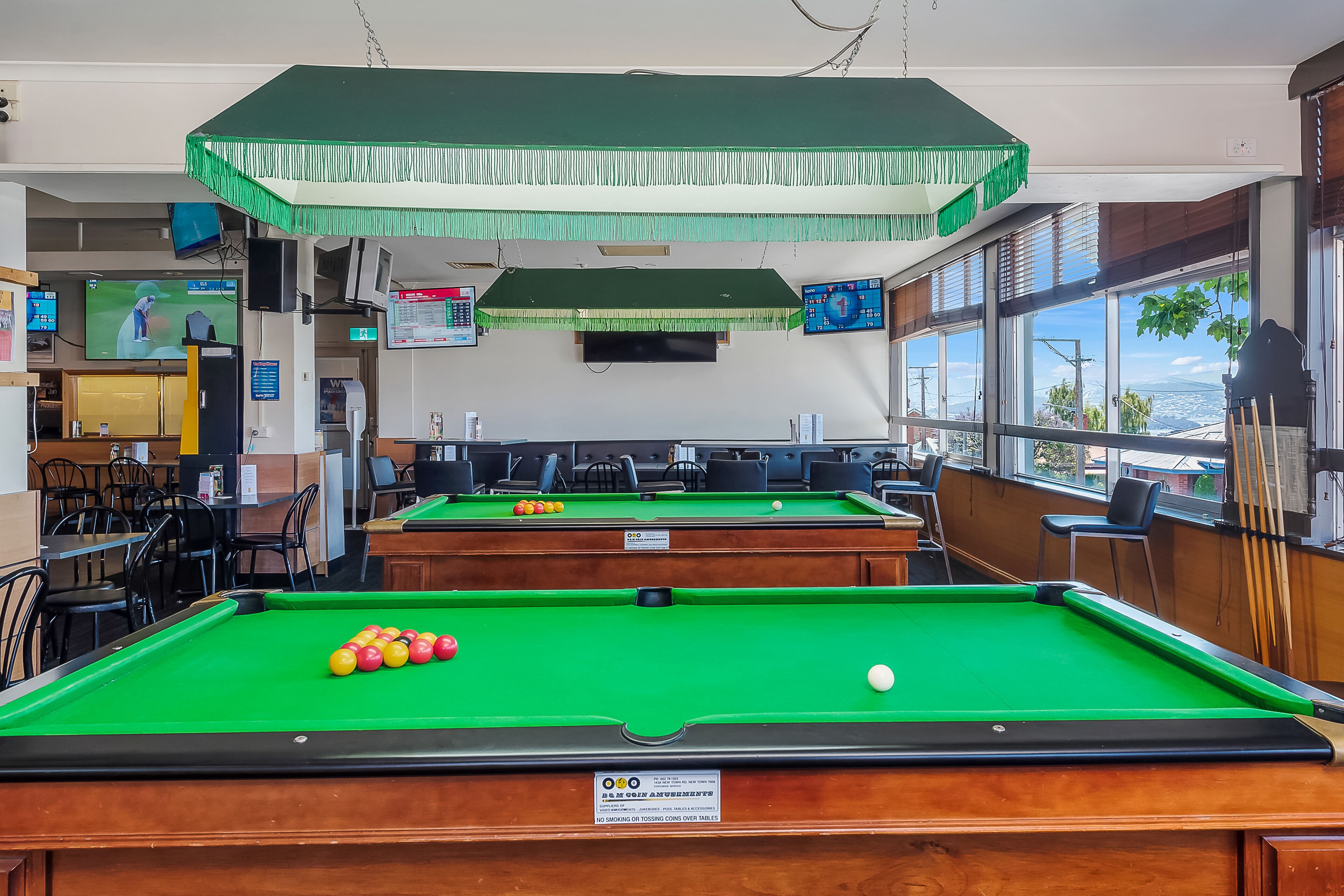A pool hall with multiple tables and a large window providing a view of the outdoors.