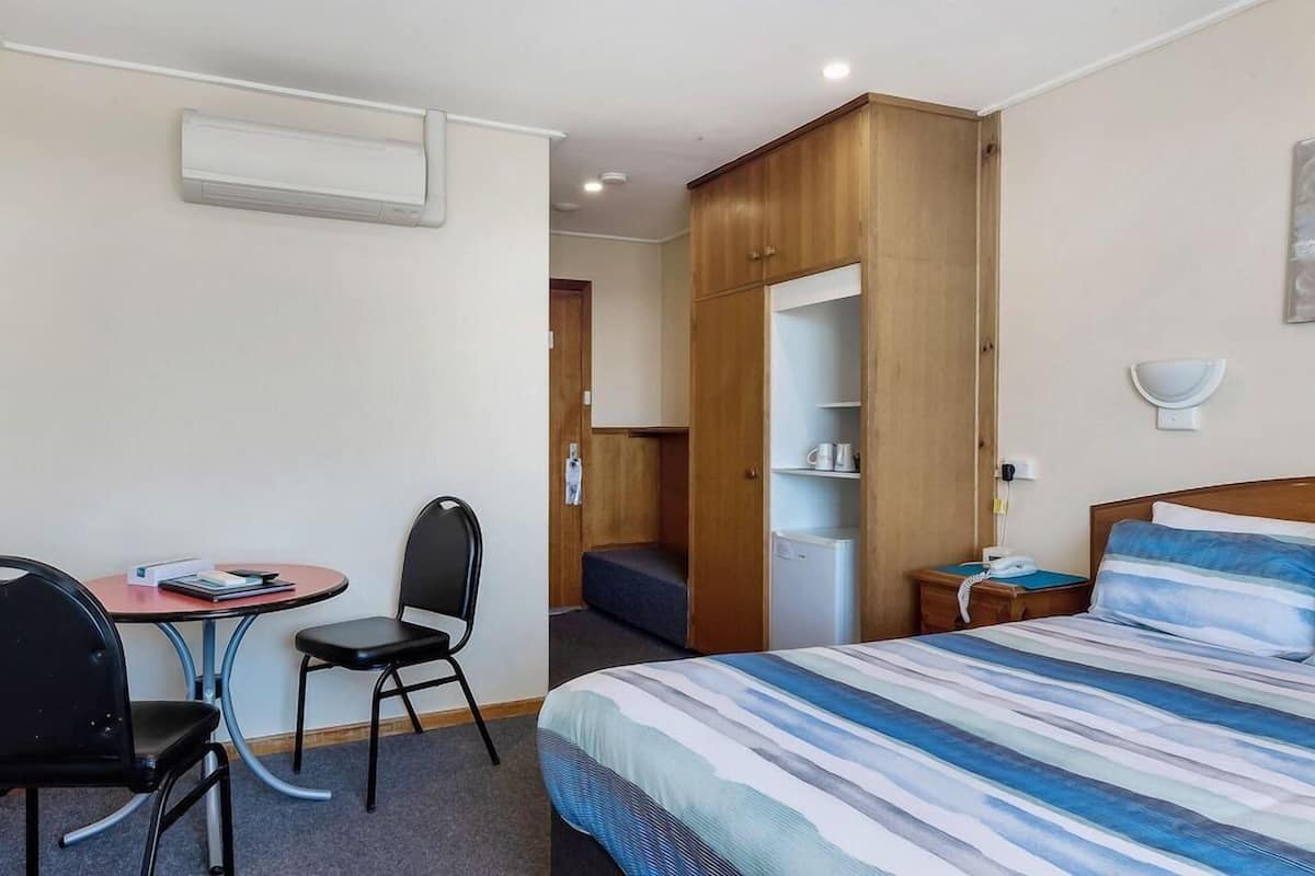 Ein Hotelzimmer mit einem Bett, einem Schreibtisch mit Stuhl, einem Kleiderschrank und einem Nachttisch.