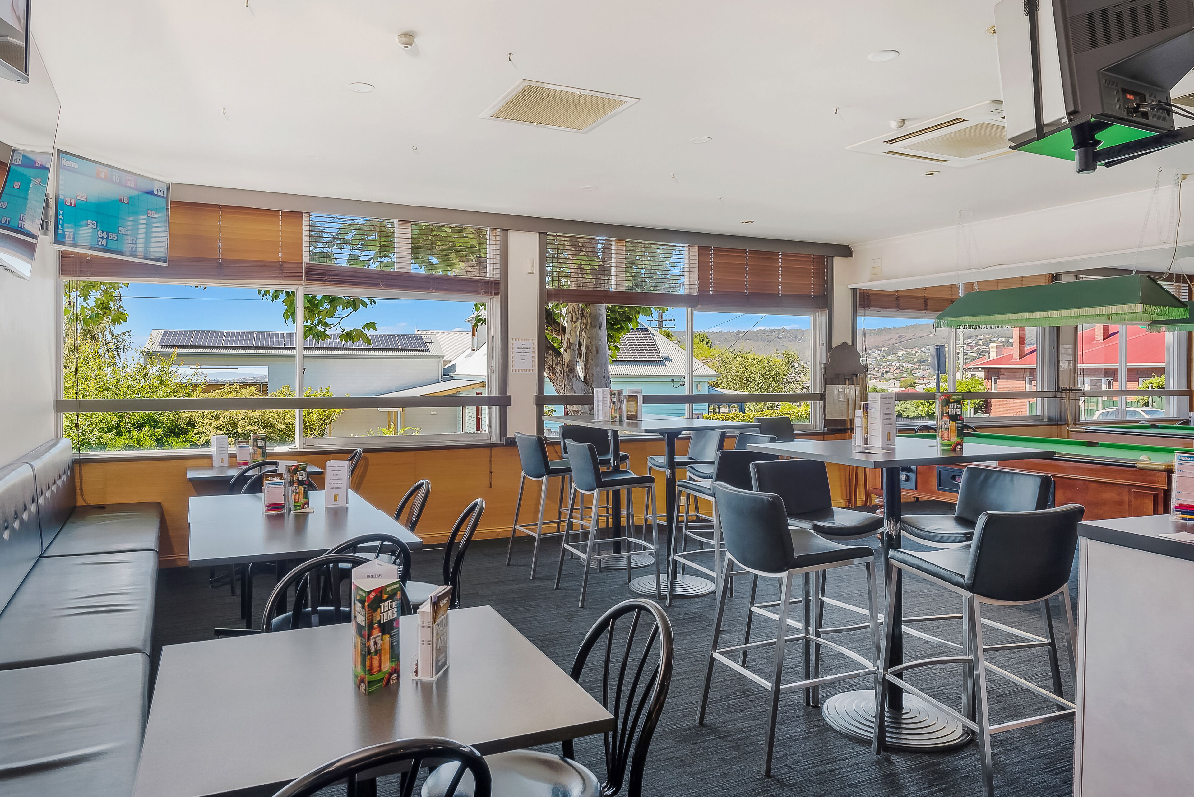 Un restaurante con mesas y sillas altas, una mesa de billar y grandes ventanales que ofrecen vistas al exterior.
