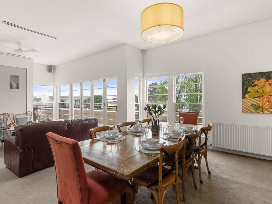 A dining area with a wooden table set for six, surrounded by wooden chairs.