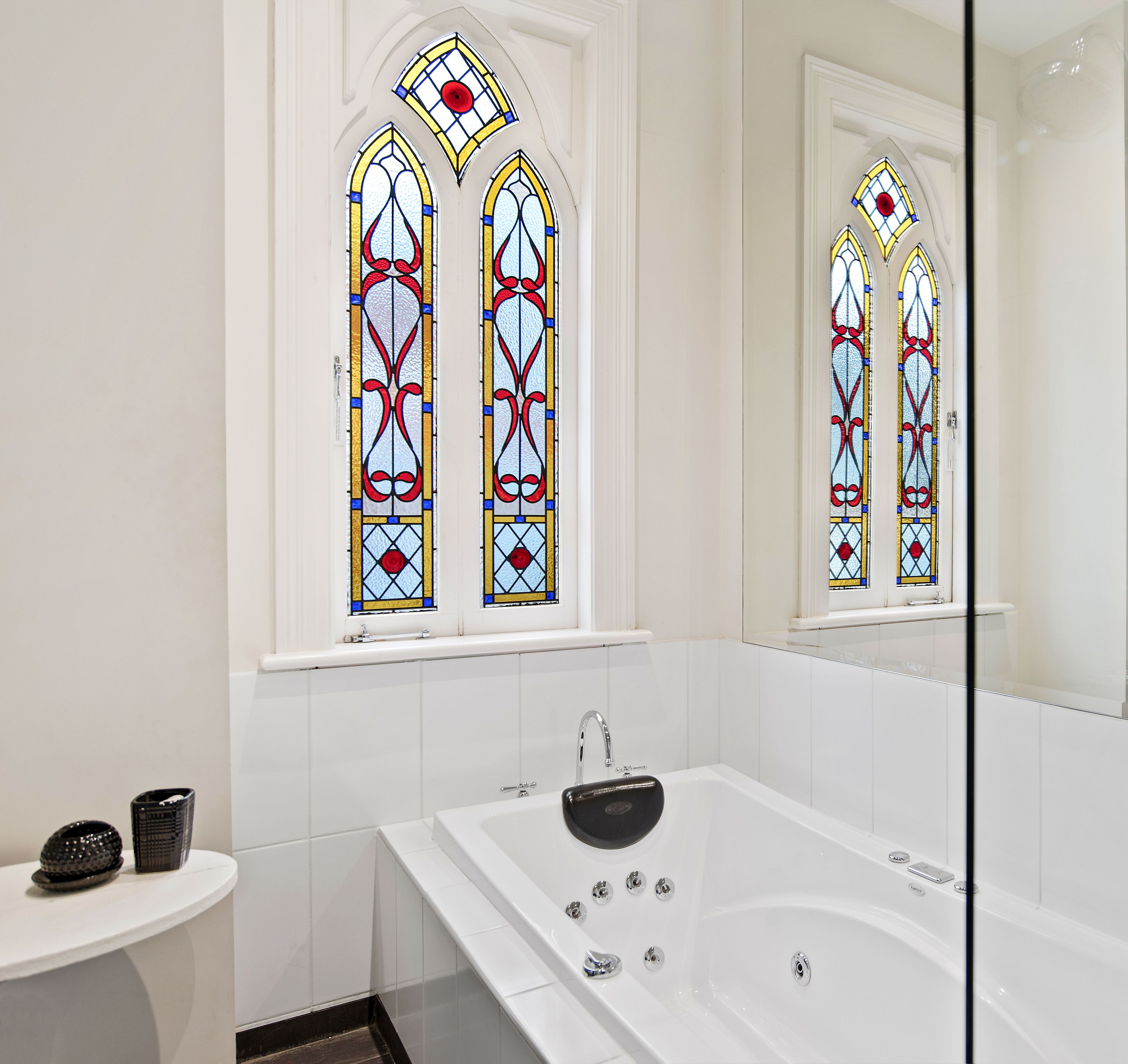 A modern bathroom with a large bathtub, a small round table, and two stained glass windows.