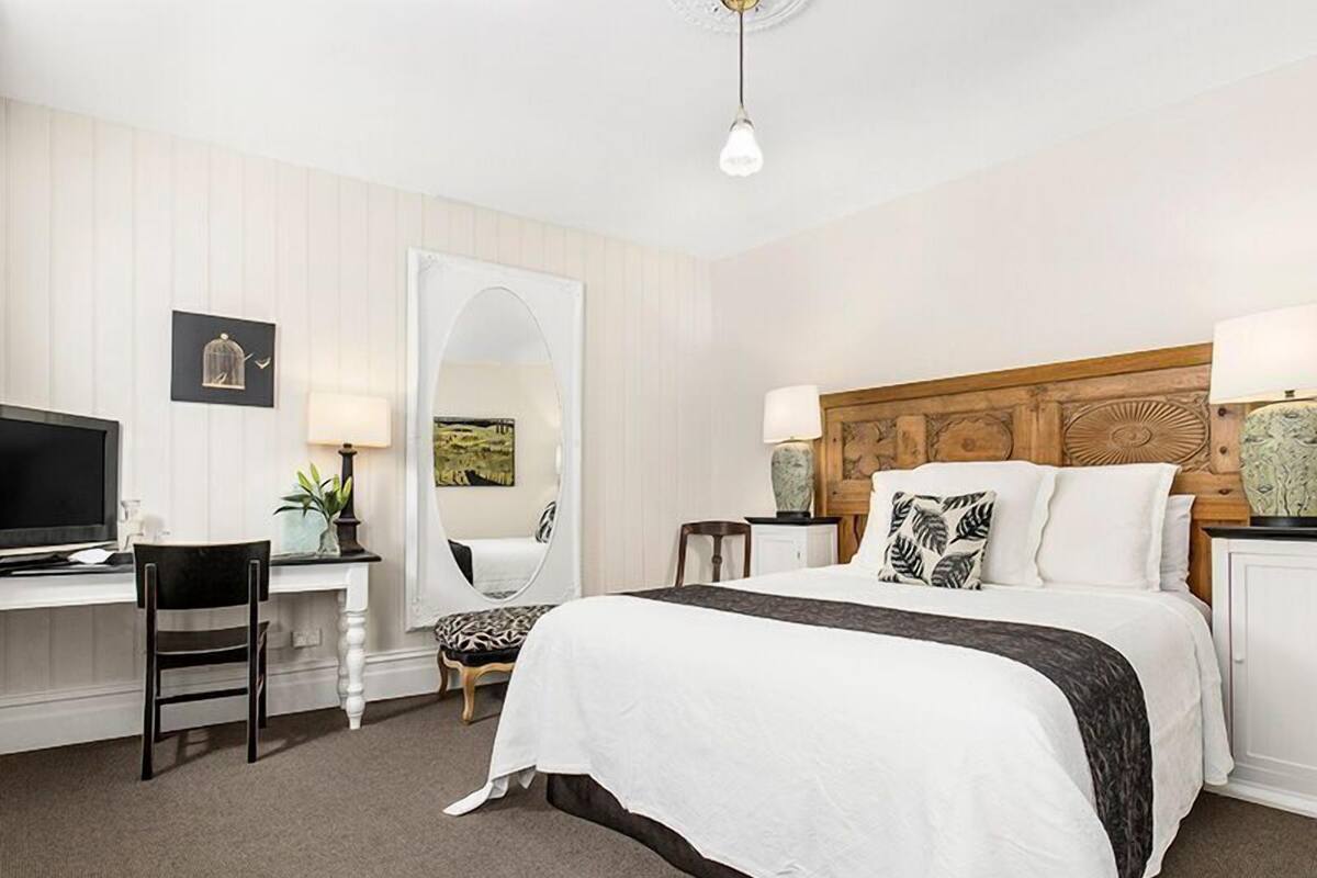 Une chambre d’hôtel équipée d’un lit, d’un bureau, d’une chaise, d’une télévision, d’un miroir et d’une lampe.
