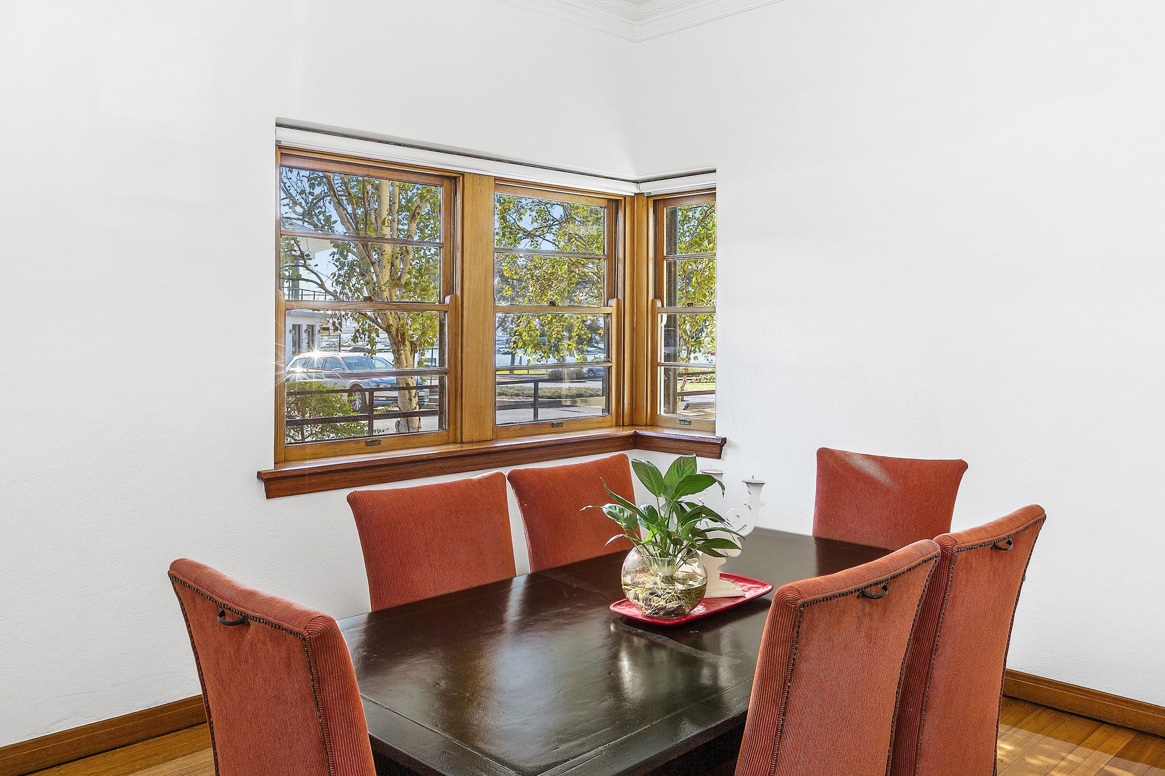 A dining area with a dark wooden table, four red upholstered chairs, and a potted plant on a red tray.