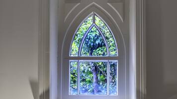 Une fenêtre dotée d’un cadre blanc et d’une arche décorative, offrant une vue sur la verdure à l’extérieur.