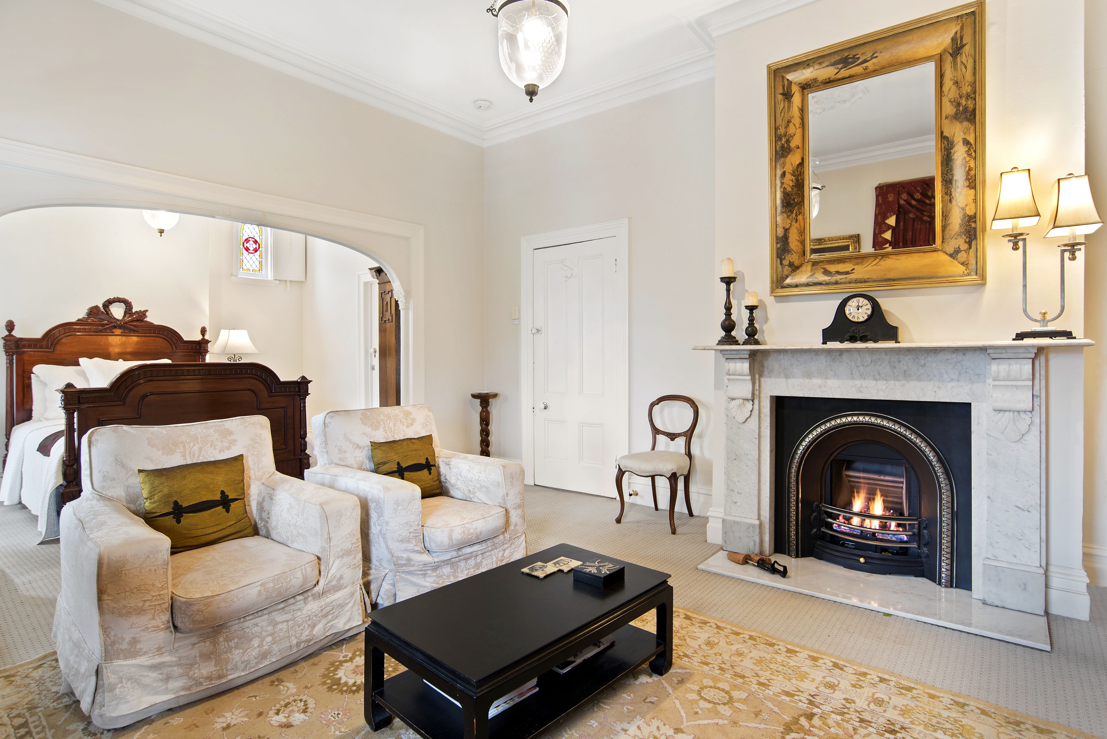A spacious living room with a fireplace, two armchairs, a coffee table, and a large mirror on the wall.