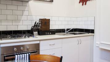 Una cocina moderna con armarios blancos, una estufa de acero inoxidable y una mesa de vidrio con un bol de naranjas.