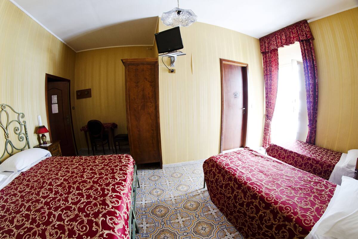 Una habitación de hotel con dos camas, un escritorio, una silla, un televisor montado en la pared y una puerta que da a otra habitación.