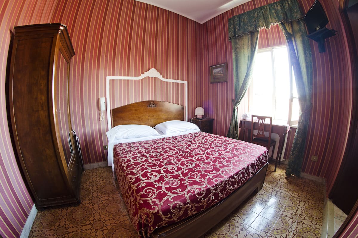 Una habitación con una cama grande, un armario de madera y una pequeña mesa con una silla.