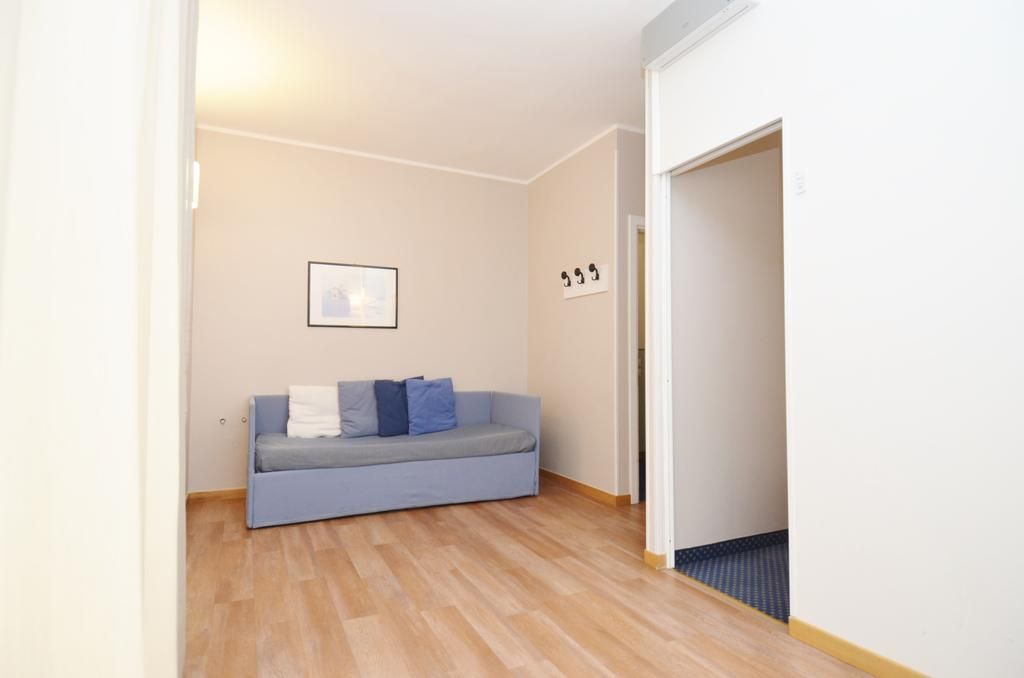 Une pièce avec un canapé de couleur claire placé contre un mur, un tableau encadré au-dessus, et une porte avec un numéro.