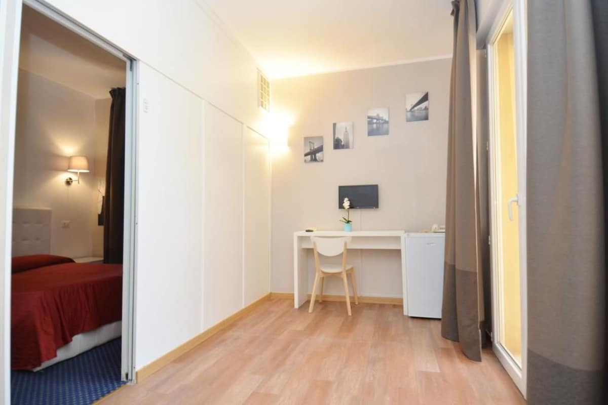 Una habitación pequeña con cama, escritorio, silla y mesita.