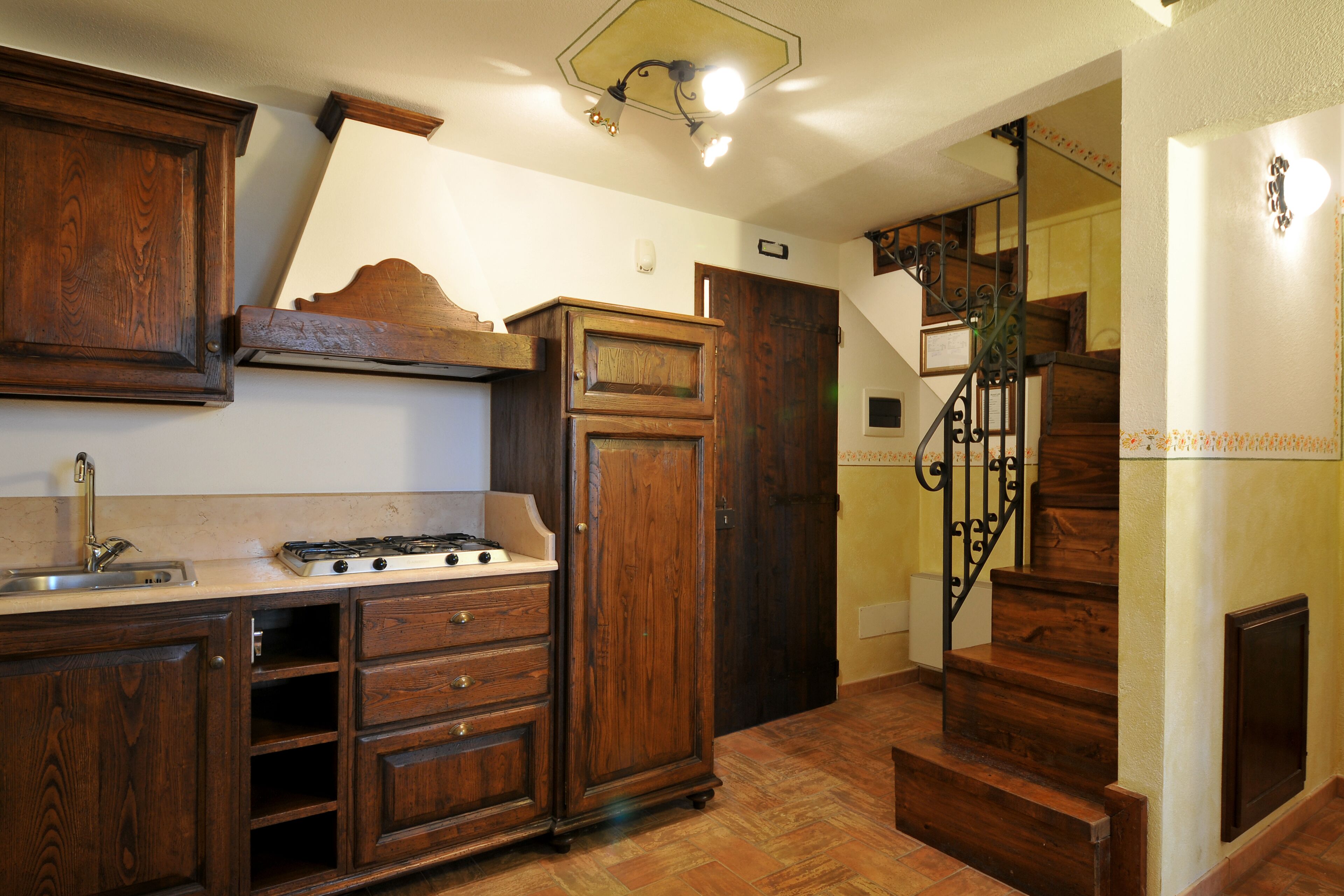 Une cuisine avec des meubles de rangement en bois, une cuisinière et un évier. On y trouve un escalier avec une rampe menant à un autre étage.