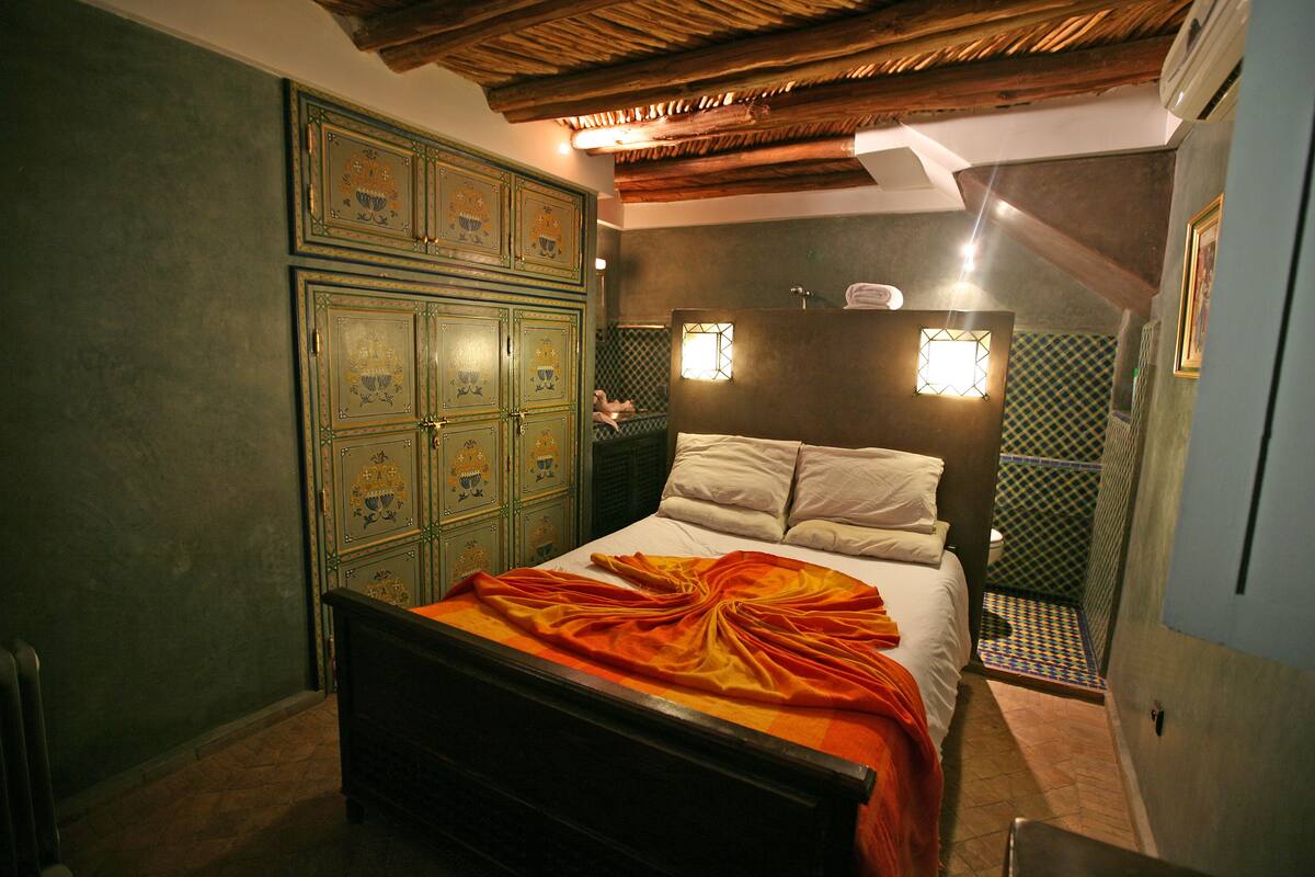 A bedroom with a wooden bed, green walls, and a tiled floor.