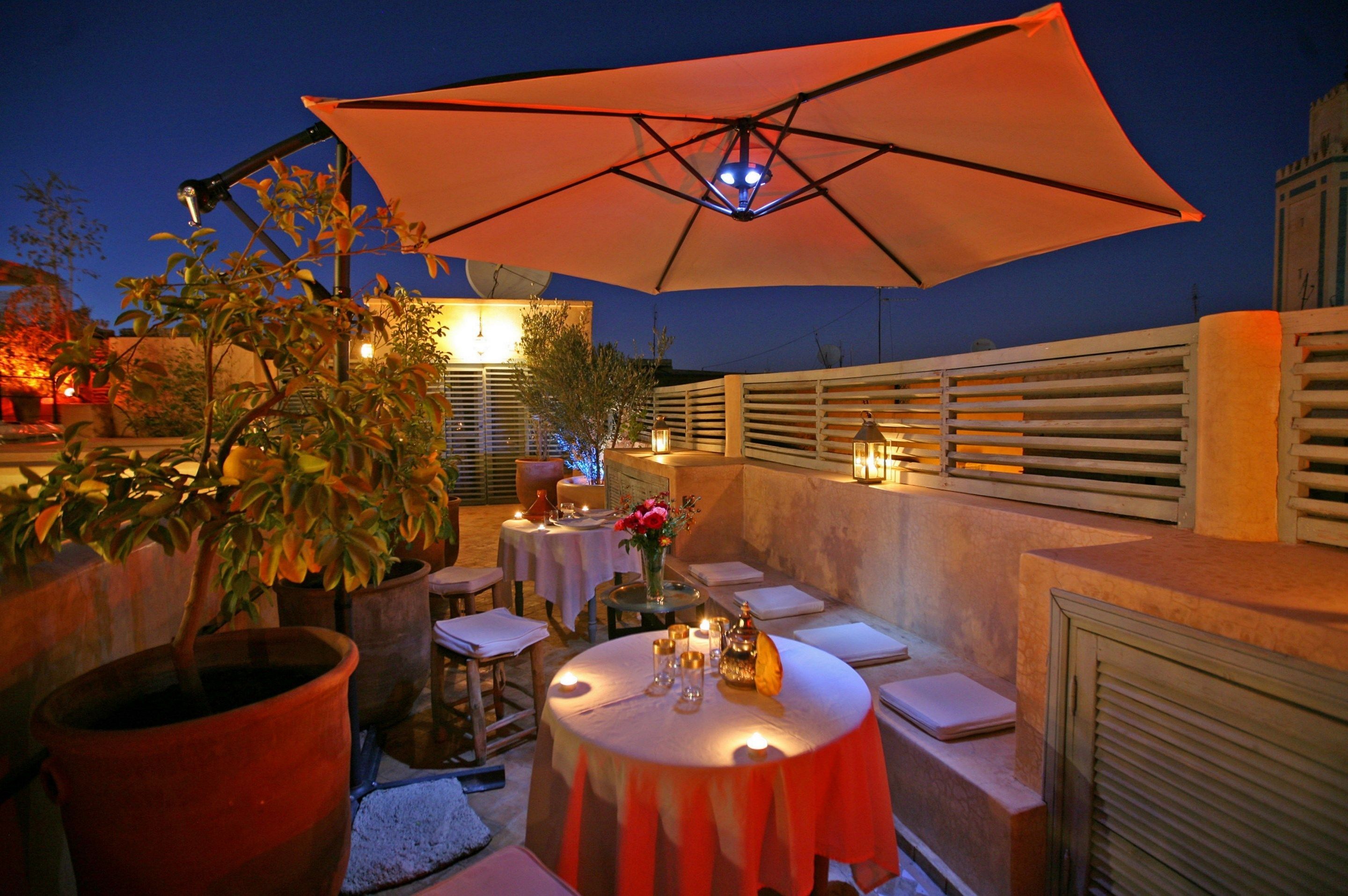 Un espace extérieur aménagé pour les repas, avec des tables, des chaises et un grand parasol.