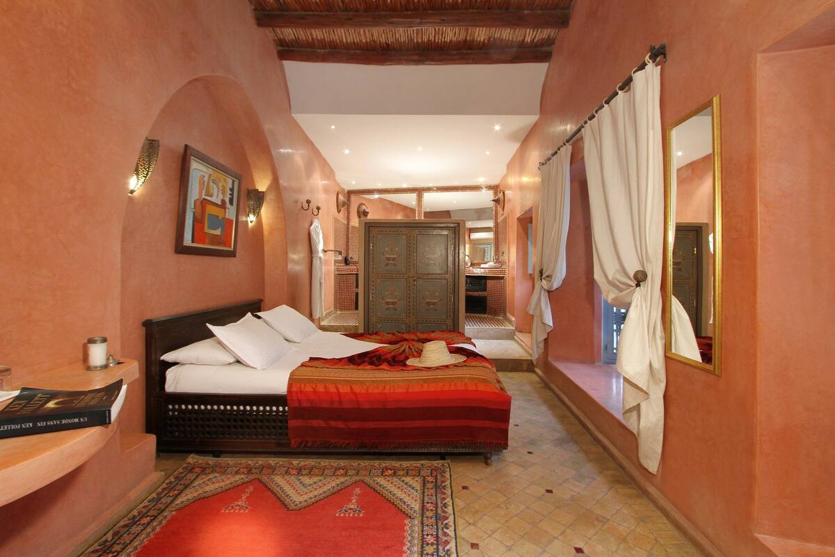 A bedroom with a bed, a nightstand, a mirror, and a door leading to another room.