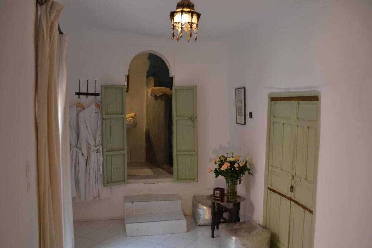 A hallway with a green door, a mirror, and a vase with flowers.