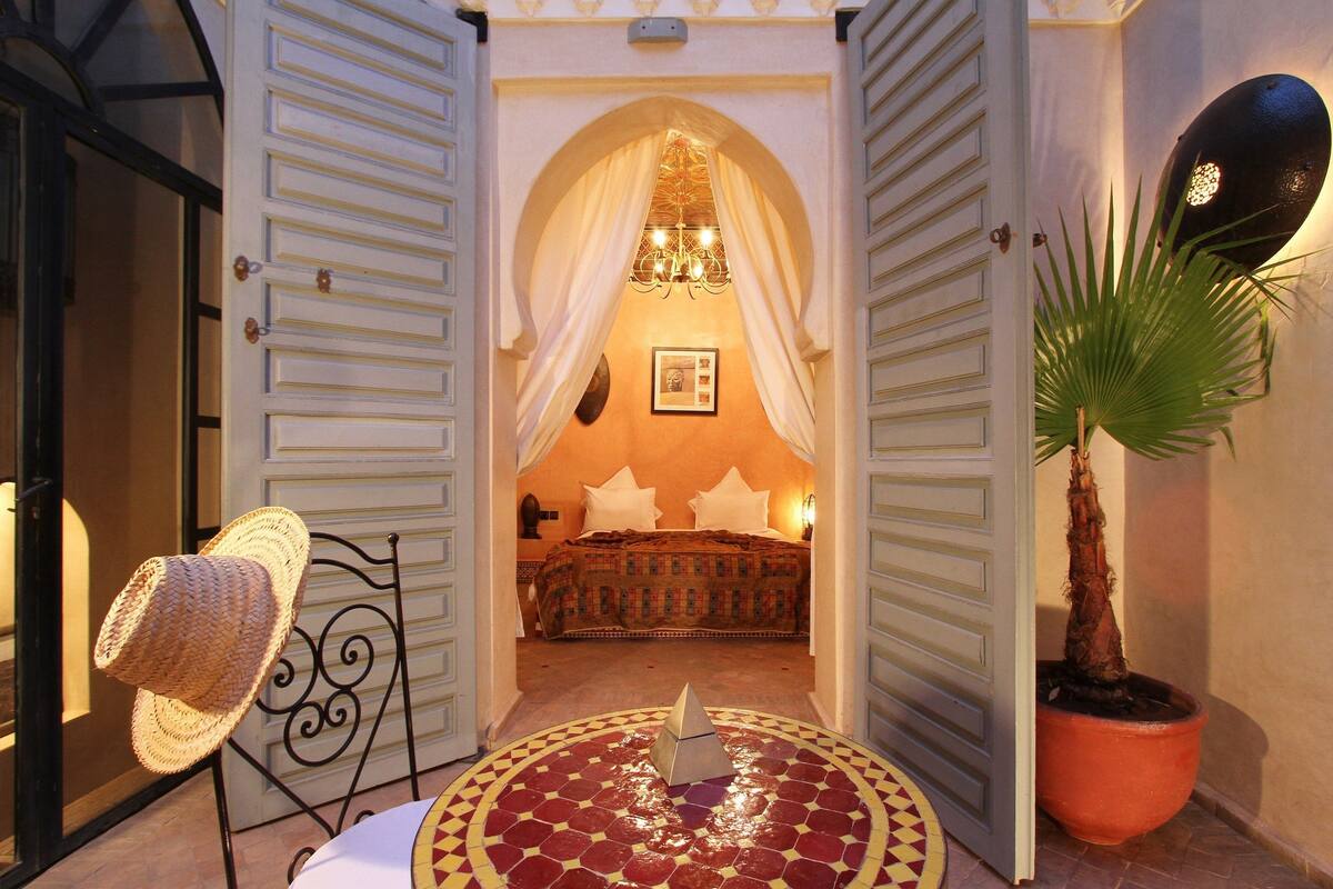 An open doorway leading to a bedroom with a bed, a chandelier, and a potted plant.