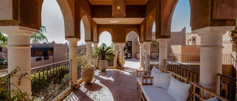 An outdoor terrace with a sofa and potted plants, surrounded by arches and columns.