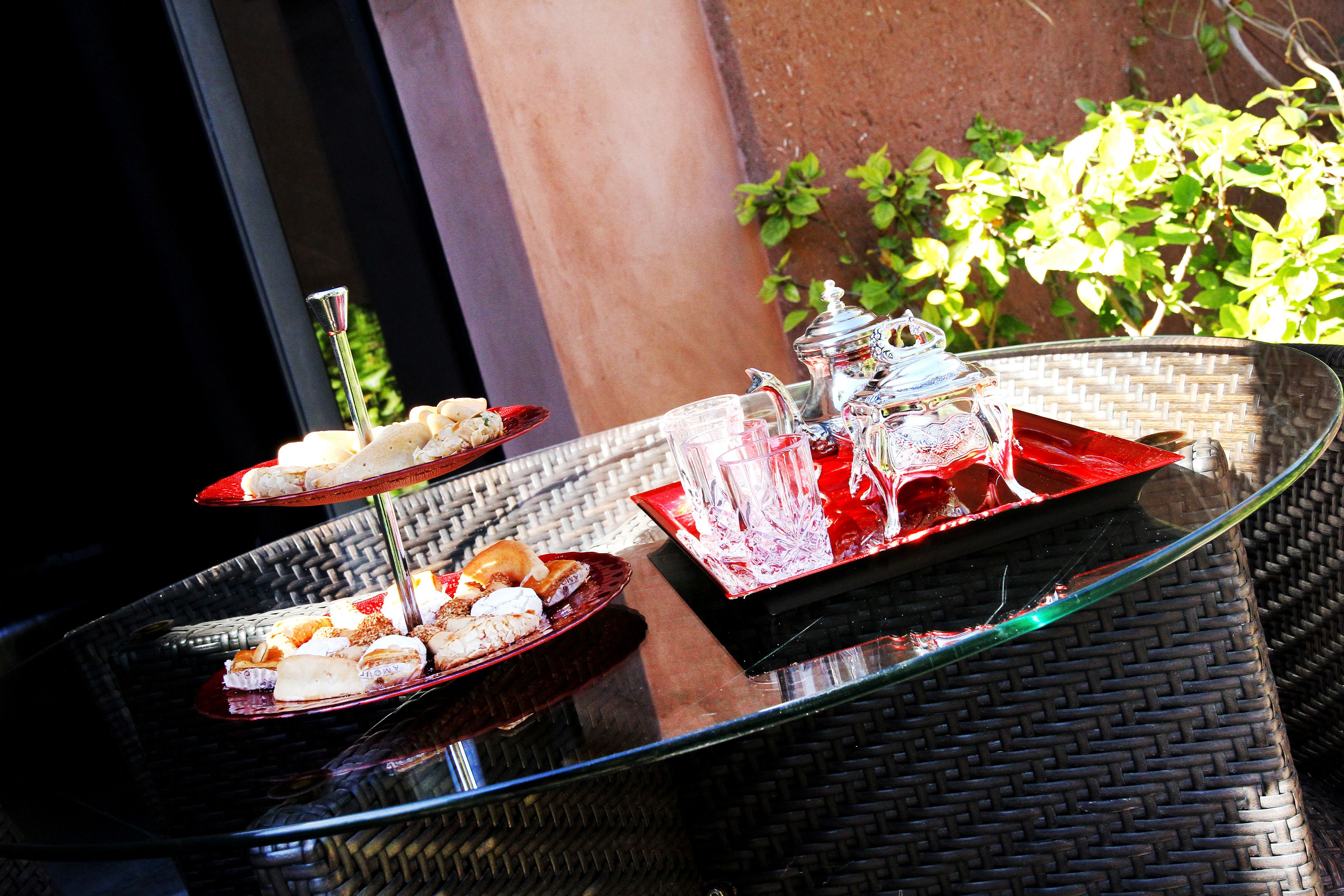 A table with glass dishes containing food and drinks, positioned outdoors with a wicker chair and a plant in the background.