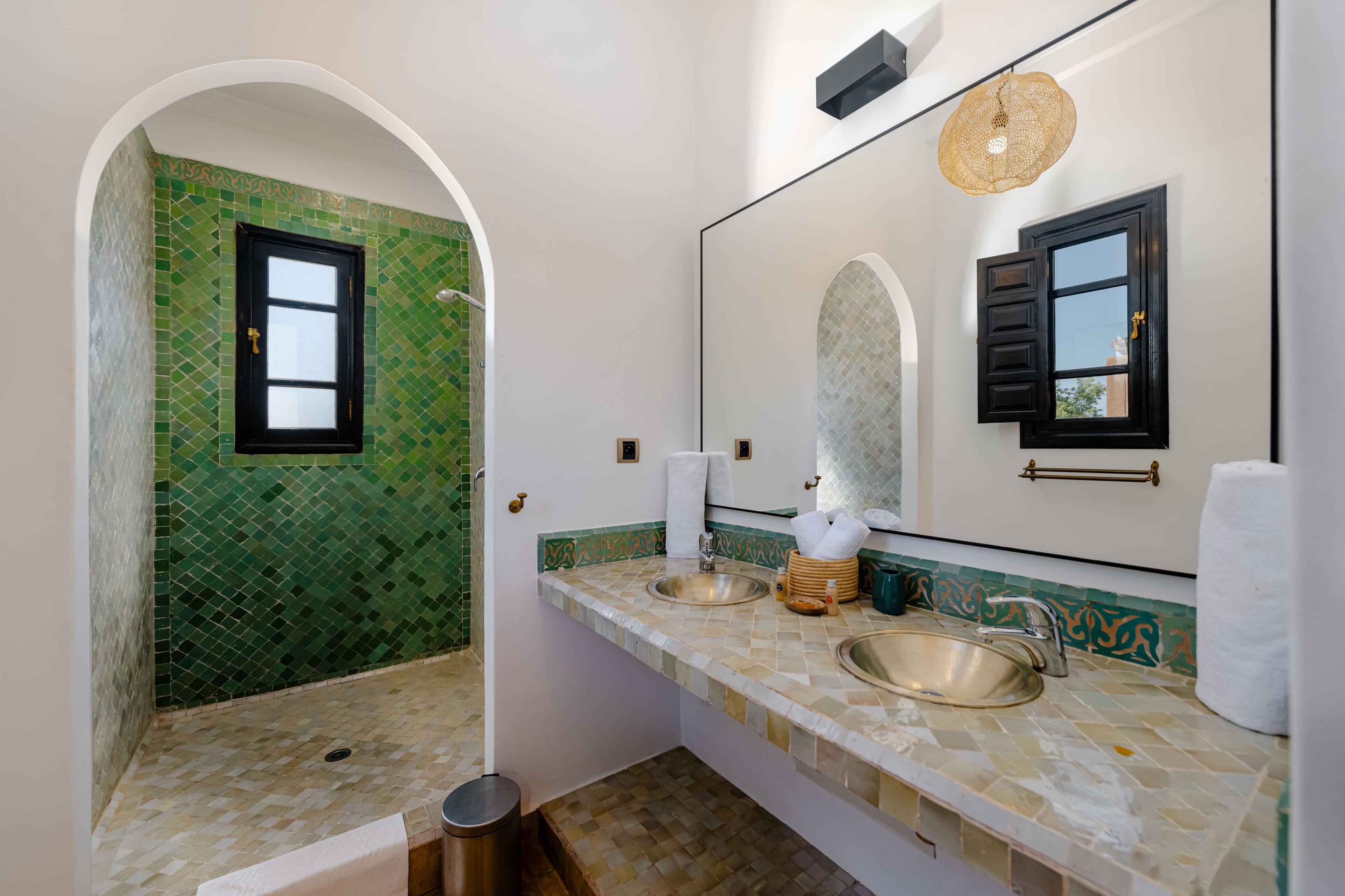 A bathroom with a green mosaic wall, a large mirror, two sinks, and a shower area.