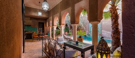 Uma área de pátio interna com vista para a piscina, com mesa de jantar, cadeiras e plantas em vasos.