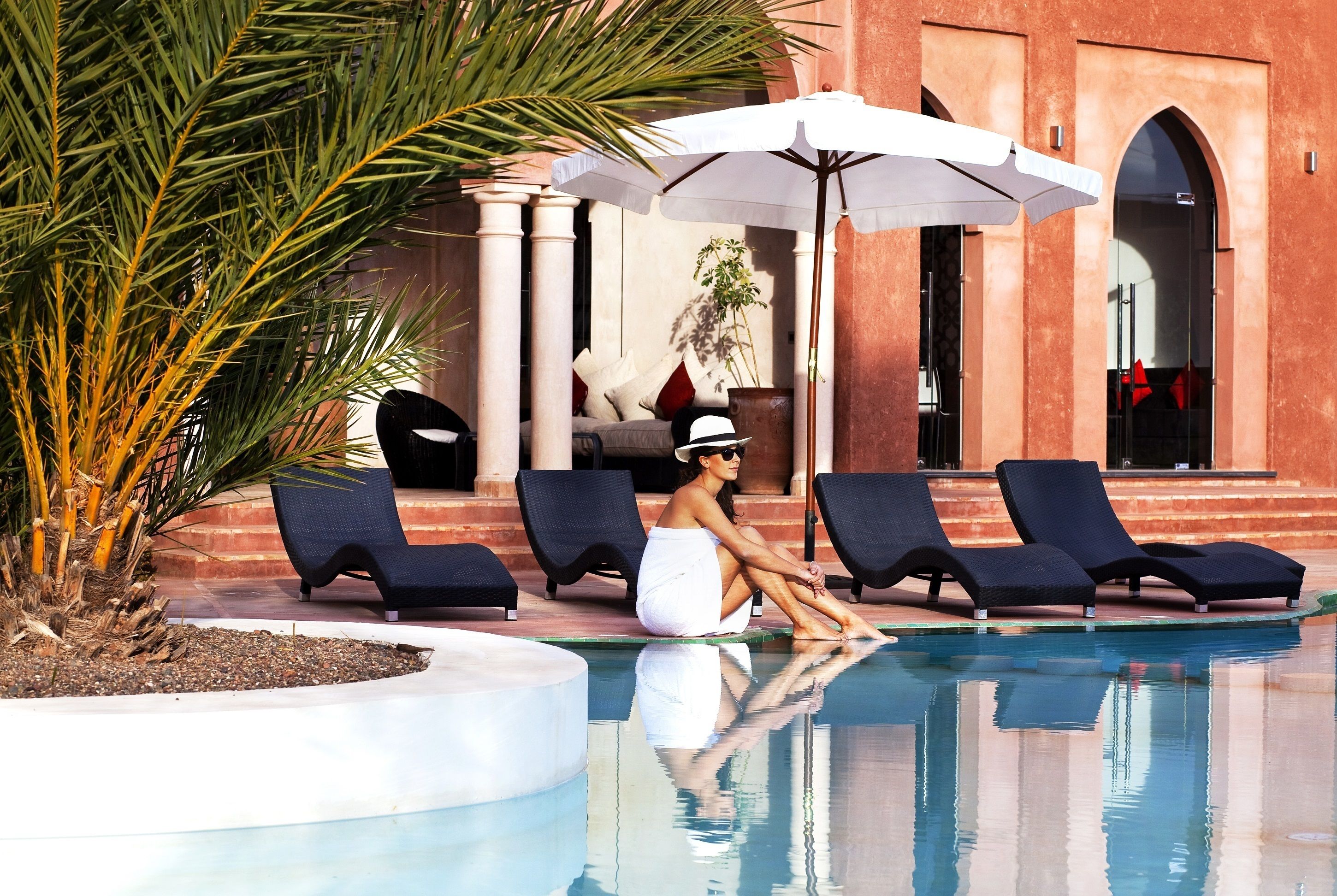 Ein Poolbereich mit Liegestühlen, einem weißen Sonnenschirm und einer Palme.