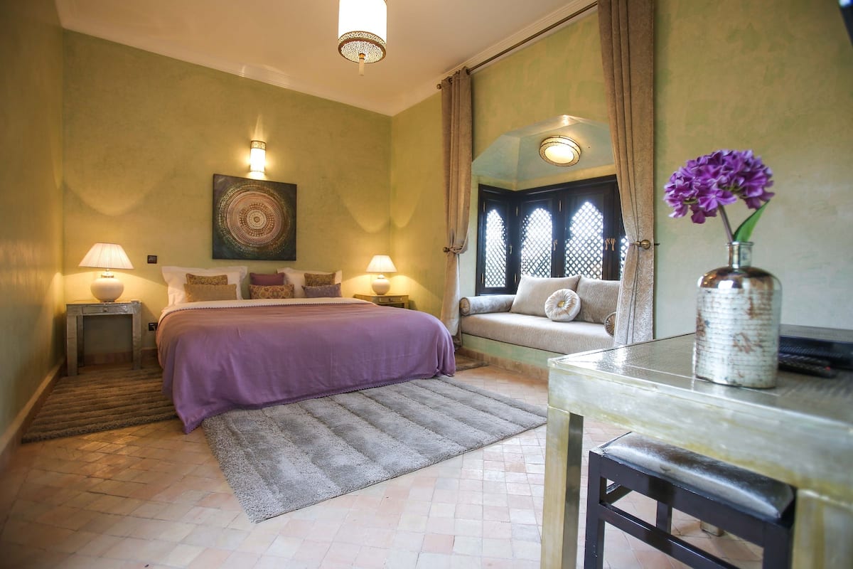 Une chambre à coucher avec un lit, des lampes de chevet, un canapé, une table en verre et un vase rempli de fleurs.