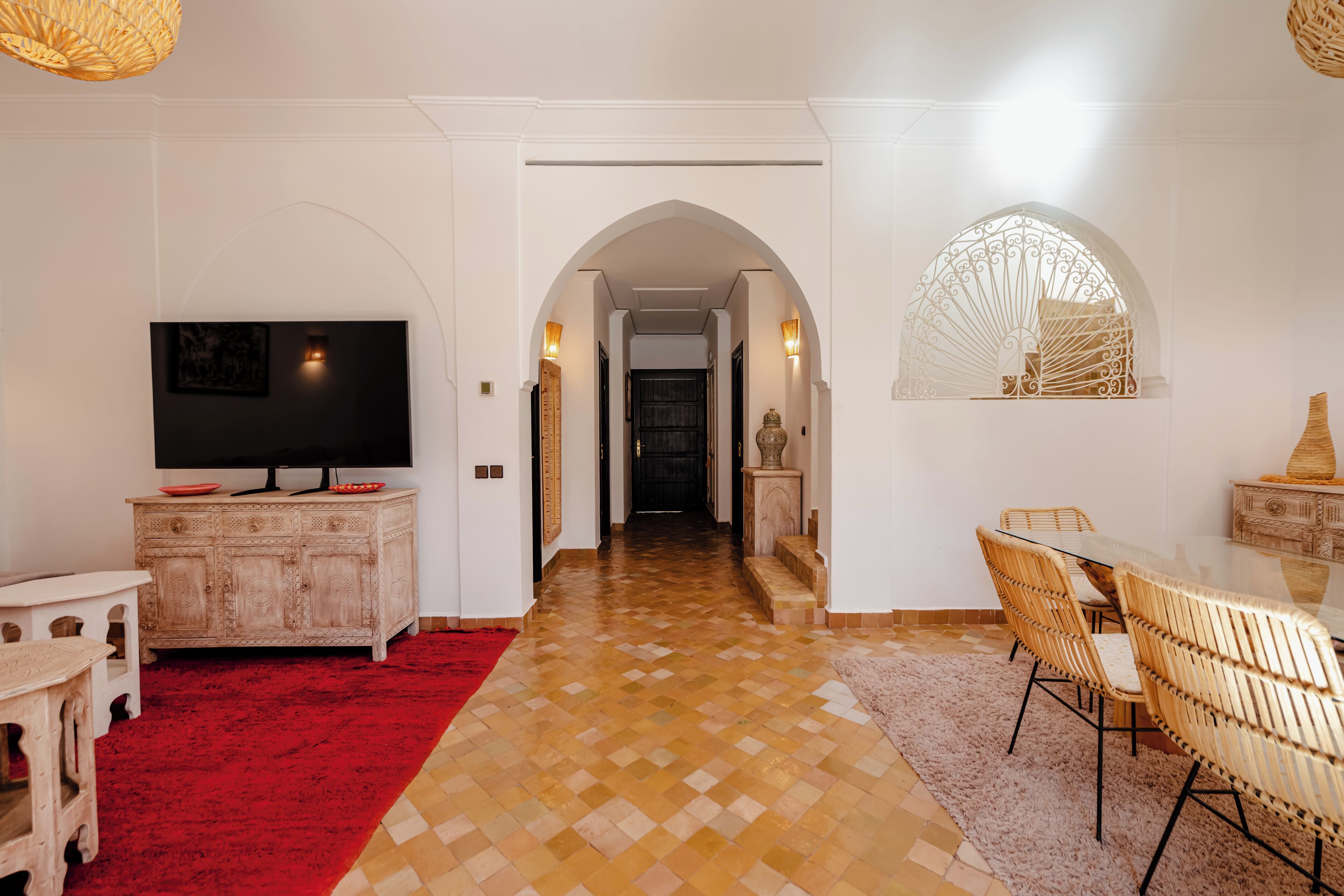 A hallway with a television, a dining area with wicker chairs, and a red carpet.