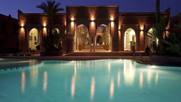 Zona de piscina con un edificio que presenta paseos con arcos y una piscina al frente.